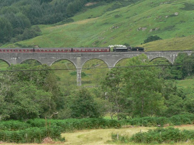 Steam train crossing the curved Glenfinnan Viaduct above Loch Shiel