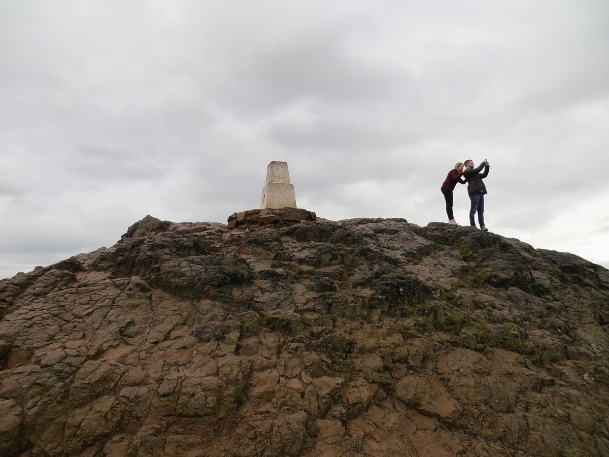 Walkers on the bare rock summit of Arthur's Seat beside the trig point, Edinburgh