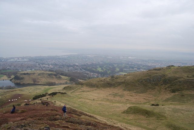Walkers descending the eastern slope of Arthur's Seat towards Dunsapie Loch, with Edinburgh and the Forth beyond