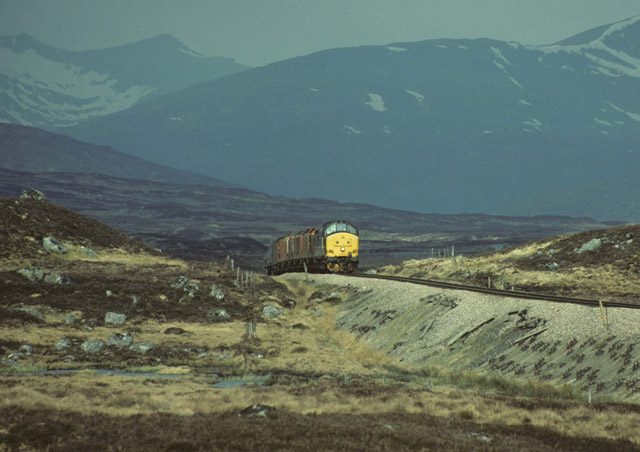 A train on the West Highland Line crossing open moor below snow-streaked hills