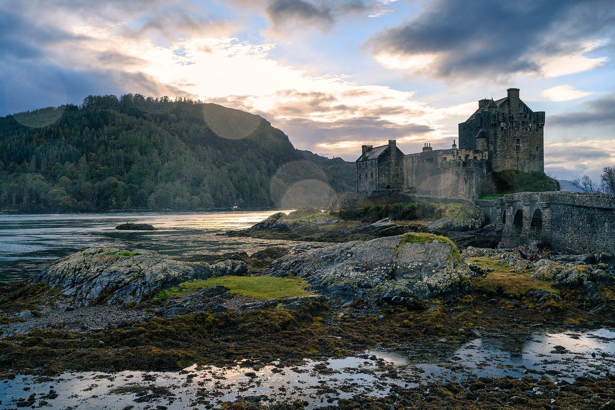 Eilean Donan Castle in low evening light from the shoreline, with the tide out
