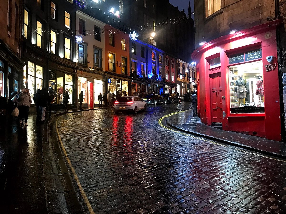 Wet cobbles and lit shopfronts on West Bow at the foot of Victoria Street, Edinburgh, after dark