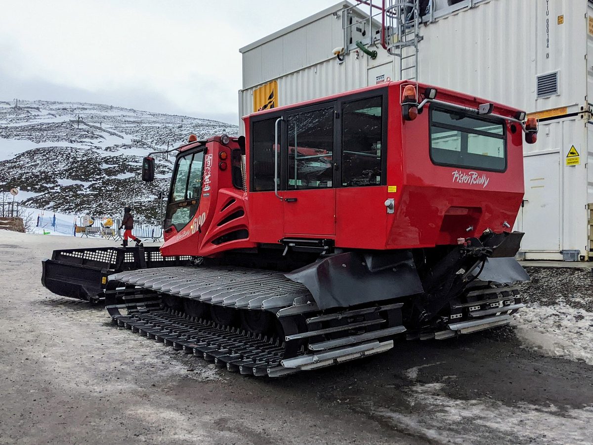 A piste groomer at Cairngorm Mountain with thin early-season snow behind