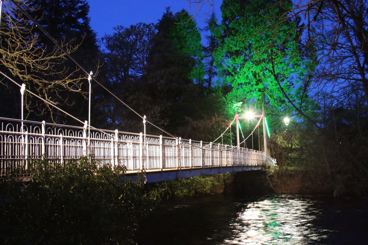 An iron suspension footbridge leading out to the wooded Ness Islands in Inverness